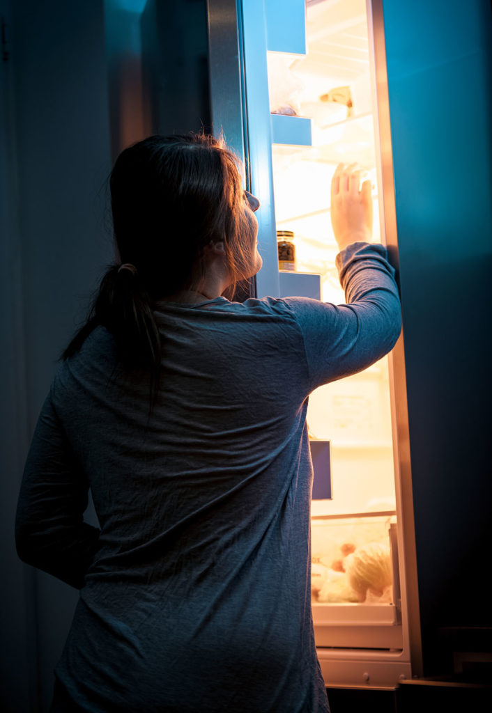 Portrait of young woman opening refrigerator at night