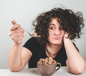 Bored woman eating cookie cereal out of a brown cup